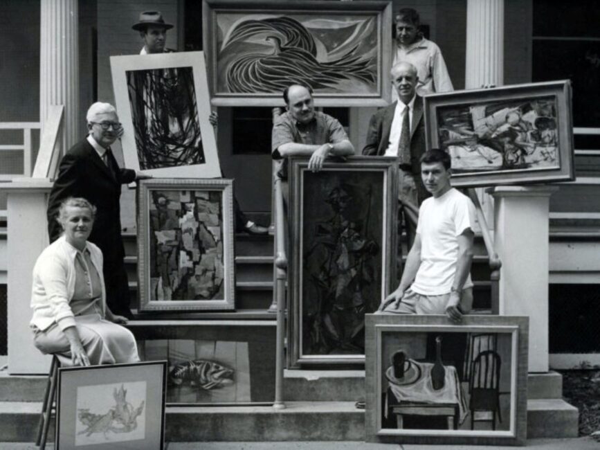 Black and white photo of adults with large framed paintings
