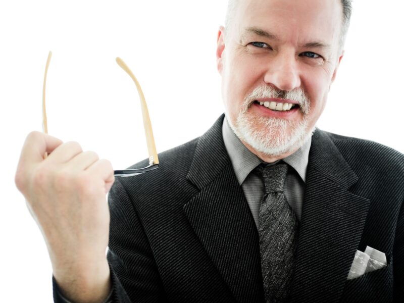 headshot of Bruce Pepich holding a pair of glasses and smiling