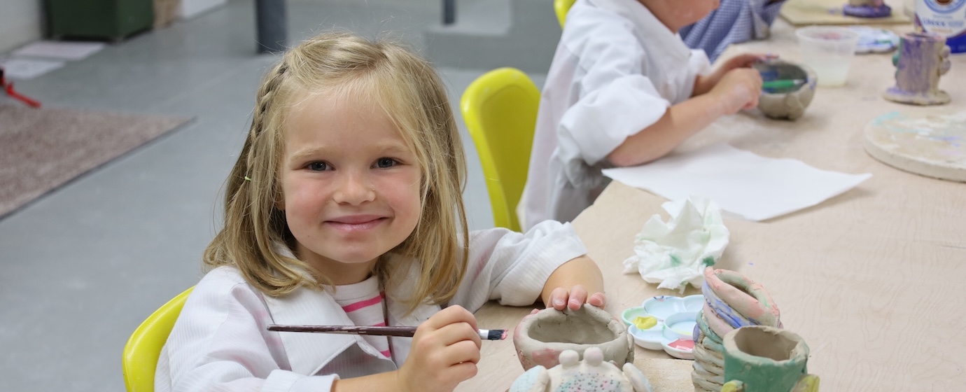 child smiling while painting a clay pot